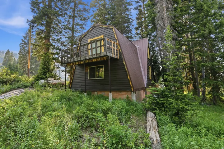 Dark-toned A-frame structure featuring a metal roof and an elevated balcony with a wood railing
