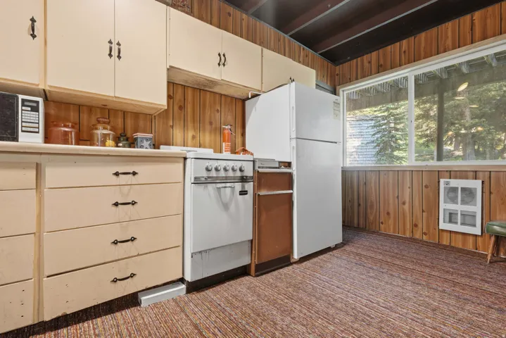 Kitchen space featuring wood paneling, a large window, light-toned cabinetry with dark hardware, a white freestanding range, and a white refrigerator