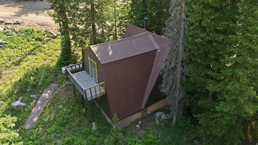 Angled contemporary cabin with a brown metal roof, featuring a raised deck with metal railings, and surrounded by mature evergreen trees