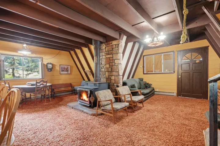 A-frame interior featuring a central stone-clad wood-burning stove, exposed ceiling beams, wood-paneled walls, and an arched top entry door