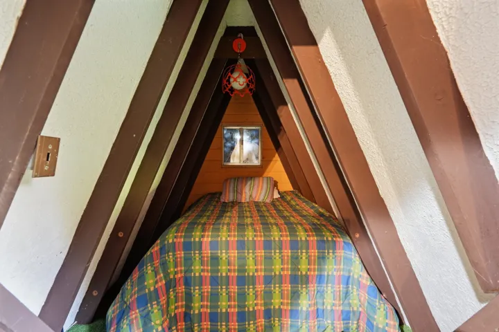 A-frame bedroom with exposed structural beams, a small window, and built-in bed platform
