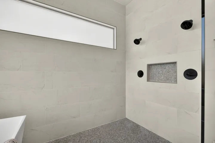 Spacious shower with large format wall tiling, matte black fixtures, an integrated tiled niche, and a mosaic tile floor