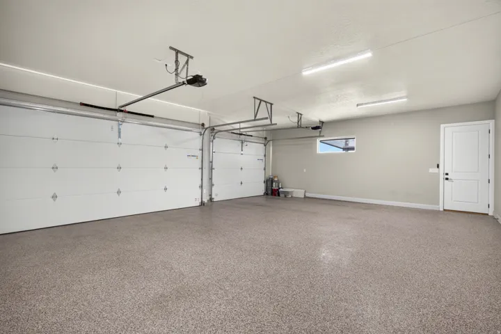 Spacious garage featuring a durable speckled epoxy floor, two overhead garage doors, overhead lighting, a white panel door, and a horizontal window