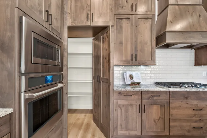 Built-in stainless steel double oven, microwave, and gas cooktop with a custom wood hood