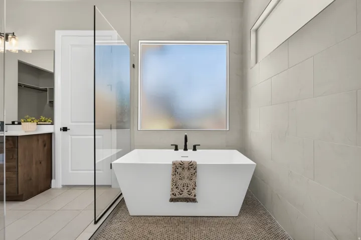Freestanding soaking tub with matte black fixtures, set against large format wall tiling and a frosted window
