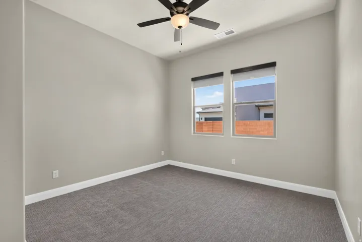 Neutral-toned room featuring a black ceiling fan with integrated lighting, two windows with roller shades, and plush grey carpeting
