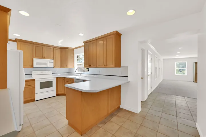 Kitchen featuring honey-toned cabinetry, light countertops, white appliances, and a tiled backsplash