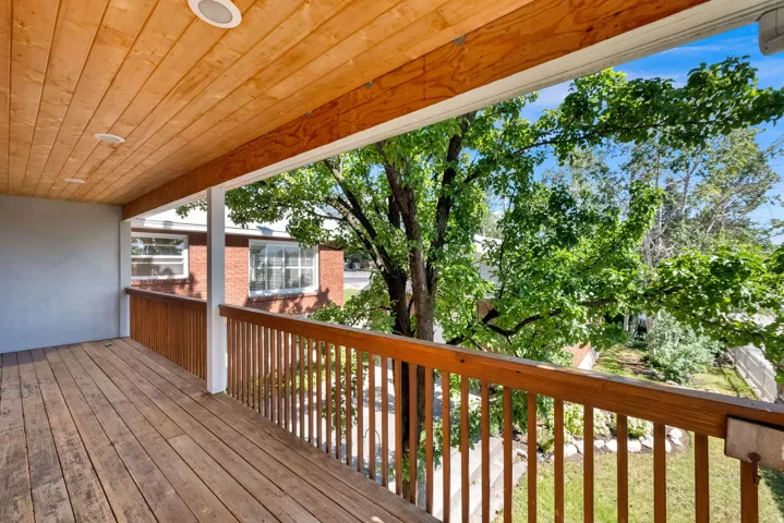 Spacious wood-finish deck with a natural wood-plank ceiling, recessed lighting, and wood railing overlooking mature trees