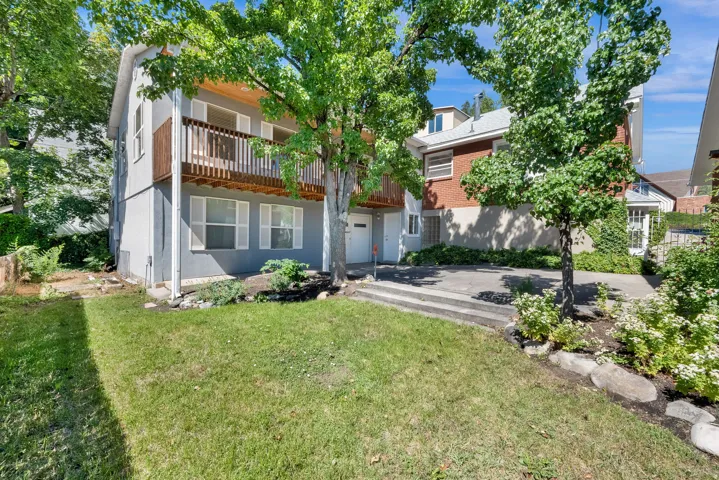 Multi-level residence featuring a gray stucco facade, white window shutters, and a wood-railed balcony