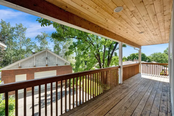 Wood-decked balcony with a natural wood ceiling, white support columns, and dark wood railings