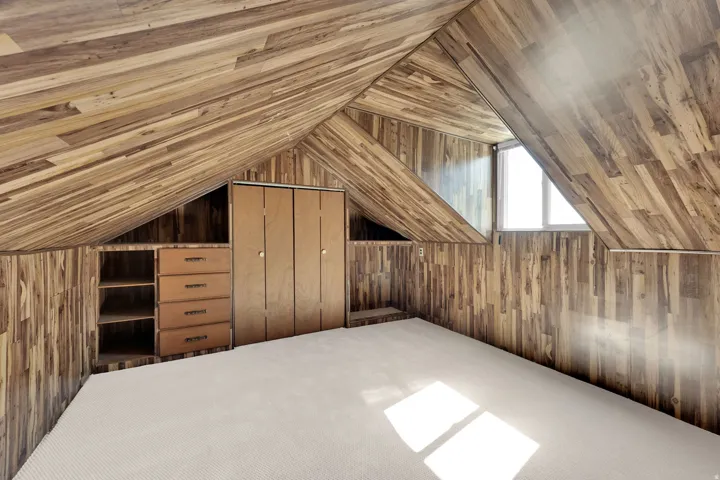 Attic space featuring wood-finish walls and sloped ceilings, a built-in closet, integrated shelving with drawers, a window, and light-toned carpeting