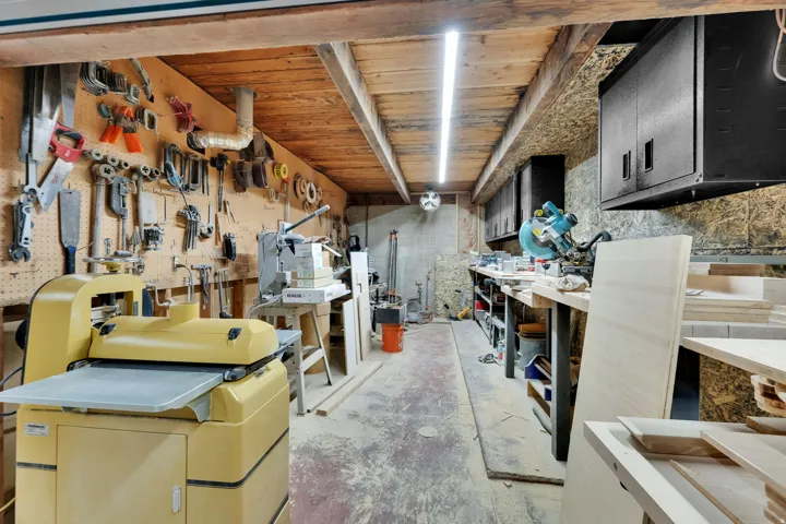 Dedicated workshop space featuring a wooden plank ceiling, exposed support beams, and concrete flooring