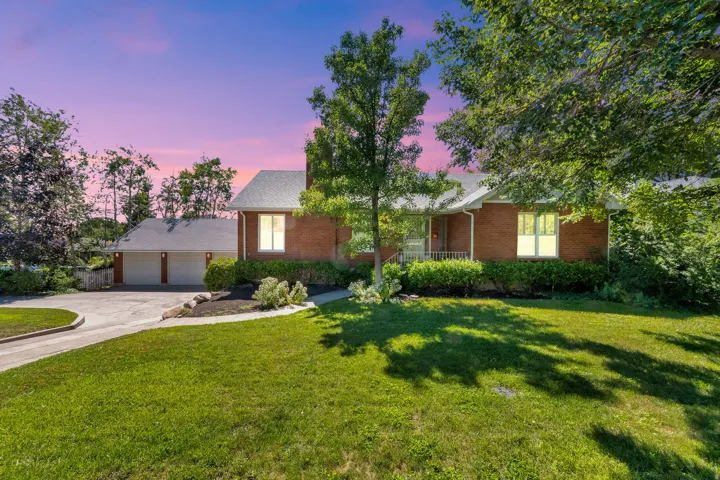 Brick exterior residence featuring a circular driveway, mature trees, manicured lawn, and an attached three-car garage