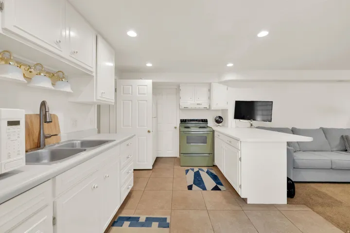Kitchenette featuring white cabinetry, a double basin stainless steel sink, a mint-green range, tile flooring, and a peninsula countertop