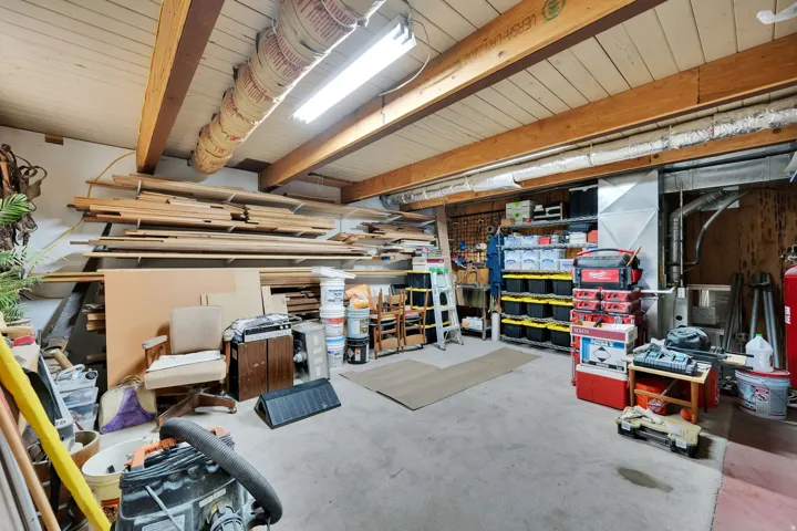 Spacious utility room featuring an open-beam ceiling, concrete flooring, and ample built-in shelving
