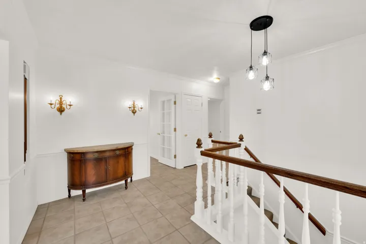 Foyer featuring neutral tile flooring, white walls with wainscoting, and crown molding
