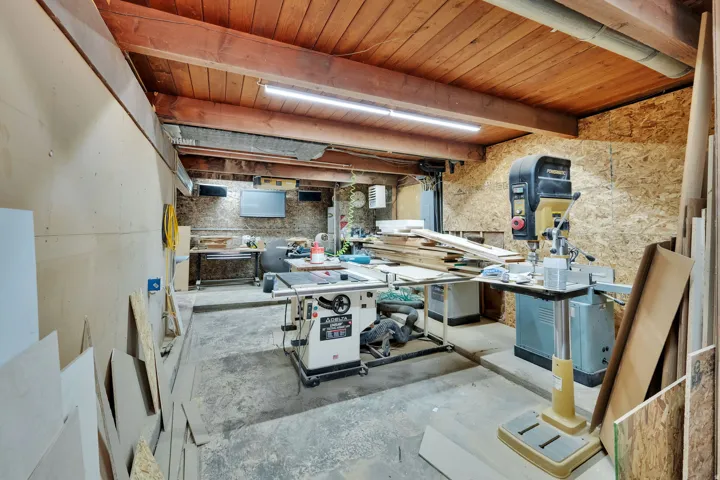 Workshop space featuring exposed wood ceiling beams and planking, raw plywood wall finishes, and concrete-finish flooring