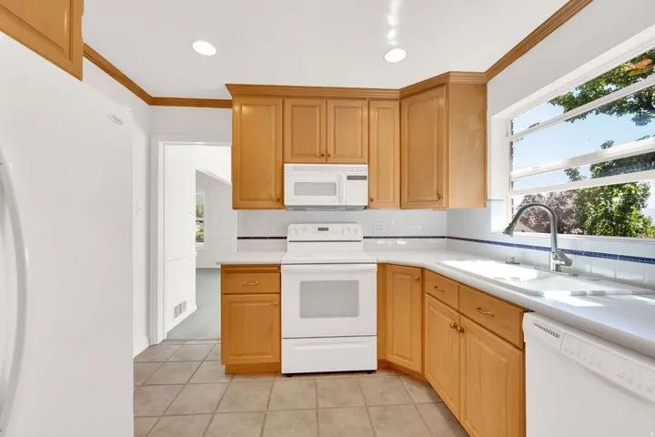 Kitchen featuring wood cabinetry, white appliances, recessed lighting, tile flooring, and a window above the sink