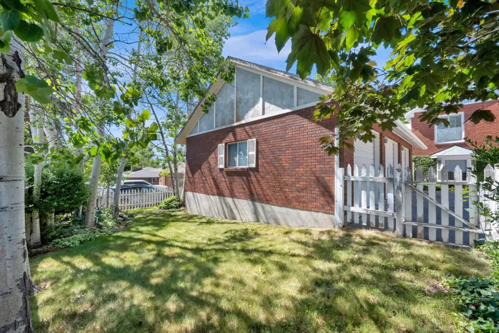 Rear exterior featuring red brick siding, a white picket fence, and mature trees providing natural shading