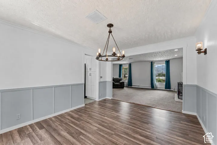 Spacious interior featuring wood-finish flooring, wainscoting with crown molding, a multi-light chandelier, and an archway opening to an additional carpeted room