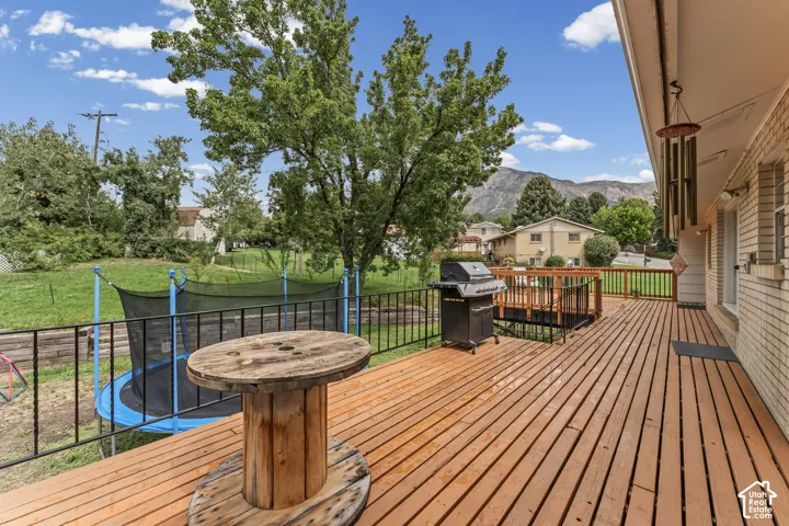 Expansive wood deck with black metal railings, featuring a mountain backdrop and a light-colored brick exterior