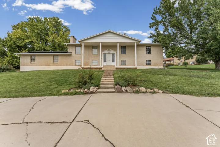 Brick exterior residence with a columned portico entrance, concrete steps, and a sloped grassy yard