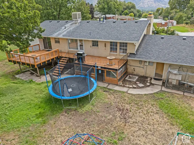 Two-tiered wooden deck with railing, brick exterior, dark shingle roofing, and a concrete patio