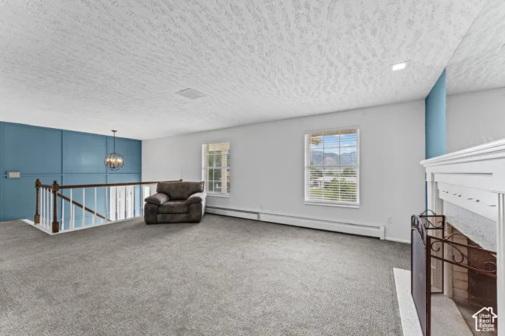 Expansive carpeted area with a decorative chandelier, white spindle railing, multiple windows, and a traditional fireplace with a white mantel
