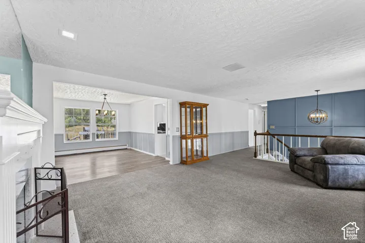 Spacious open-concept living area featuring a white fireplace with an ornate screen, gray carpeting, a decorative blue accent wall with paneling, and a contemporary spherical pendant light fixture