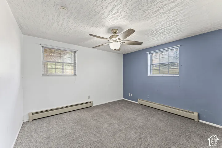 Room with gray textured carpeting, a ceiling fan with integrated lighting, and two windows with blinds