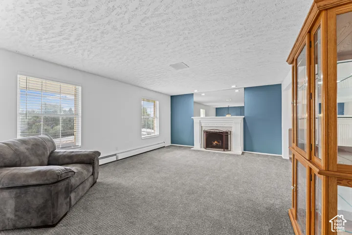 Carpeted living area featuring a white fireplace with a metal grate, a built-in wooden display cabinet with glass panels, and multiple windows