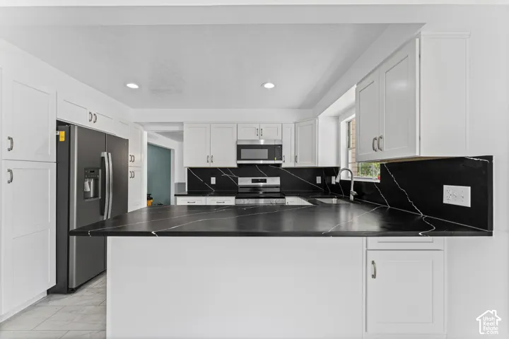 Kitchen featuring white cabinetry, dark countertops with light veining, a stainless steel refrigerator, a stainless steel microwave, and recessed lighting