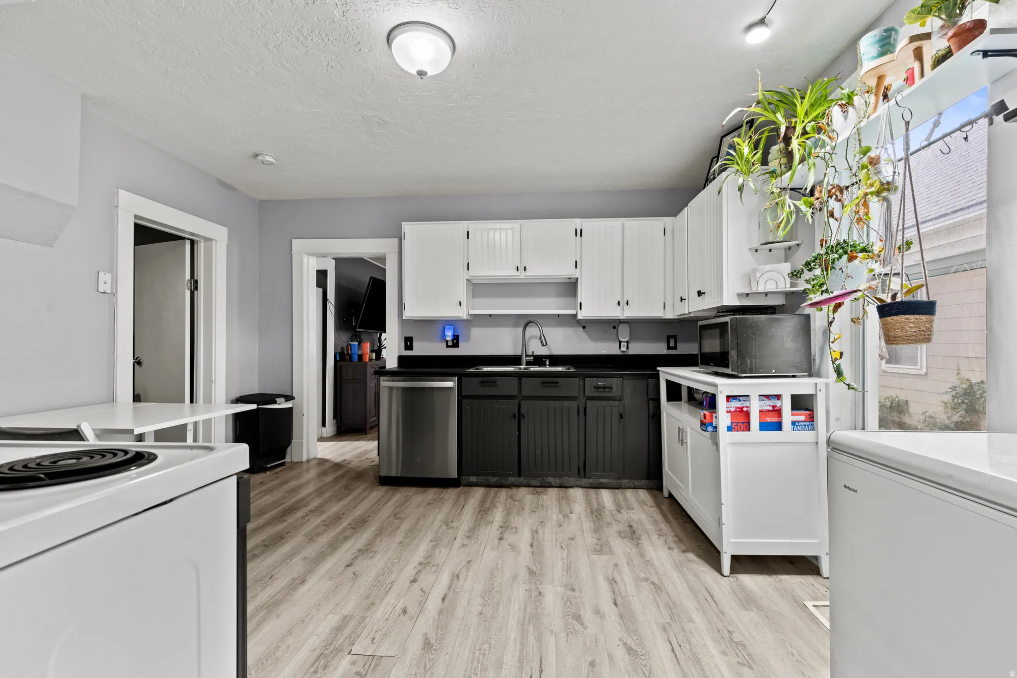 Kitchen featuring wood-finish flooring, two-tone cabinetry with white upper and dark lower units, a stainless steel dishwasher, and a window providing natural light
