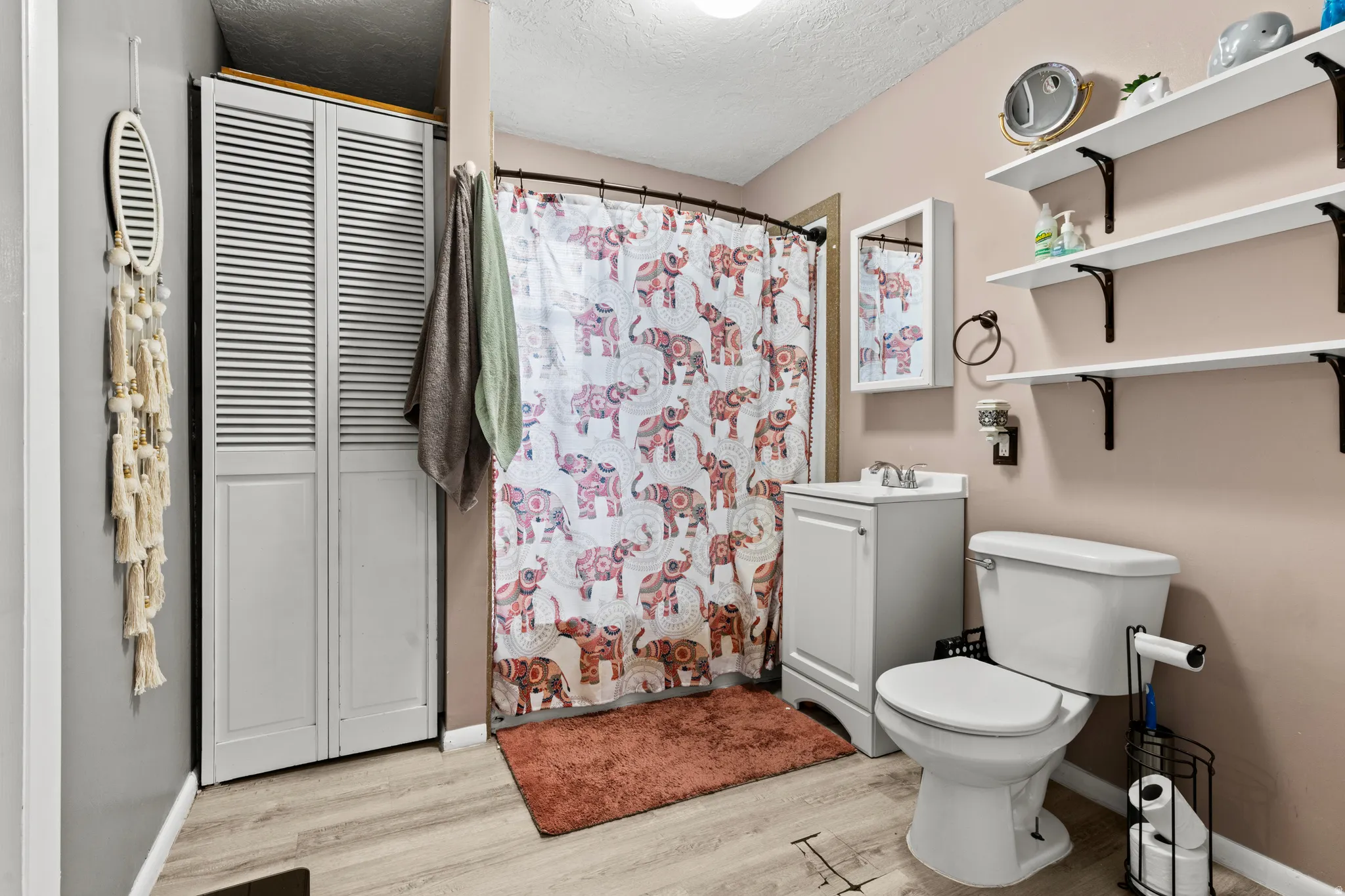 Bathroom with wood-finish flooring, a white vanity with integrated sink, and white shelving with dark brackets