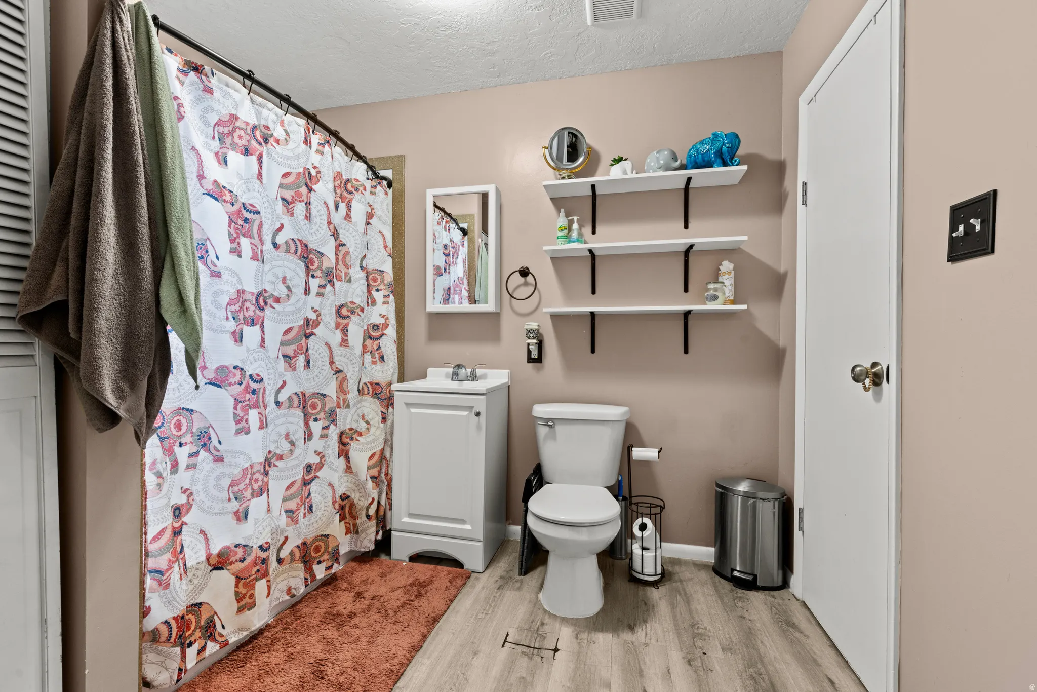 Full bathroom featuring a white vanity with integrated sink, wood-finish flooring, and white floating shelves with black brackets