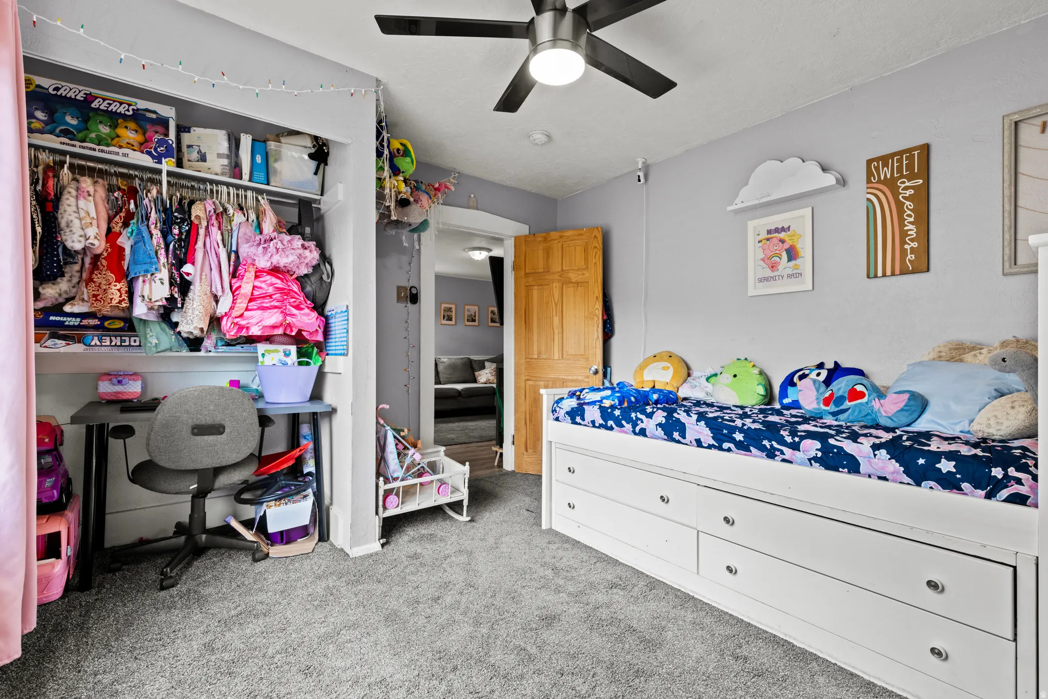 Carpeted room featuring a ceiling fan with integrated lighting, a built-in closet with shelving and hanging rods, a light wood-finish door, and pale gray wall finishes