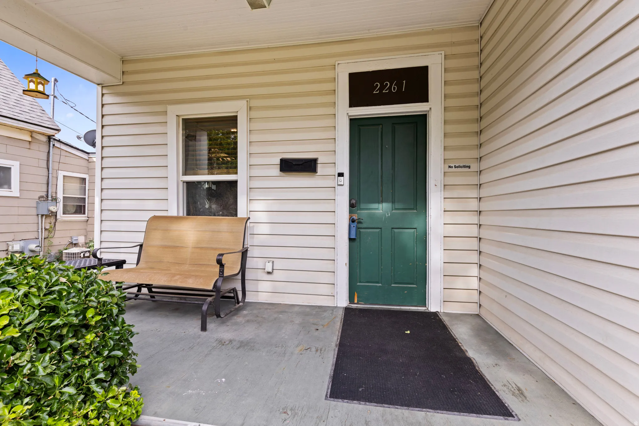 Covered front porch featuring cream-colored siding and a dark green entry door with transom window