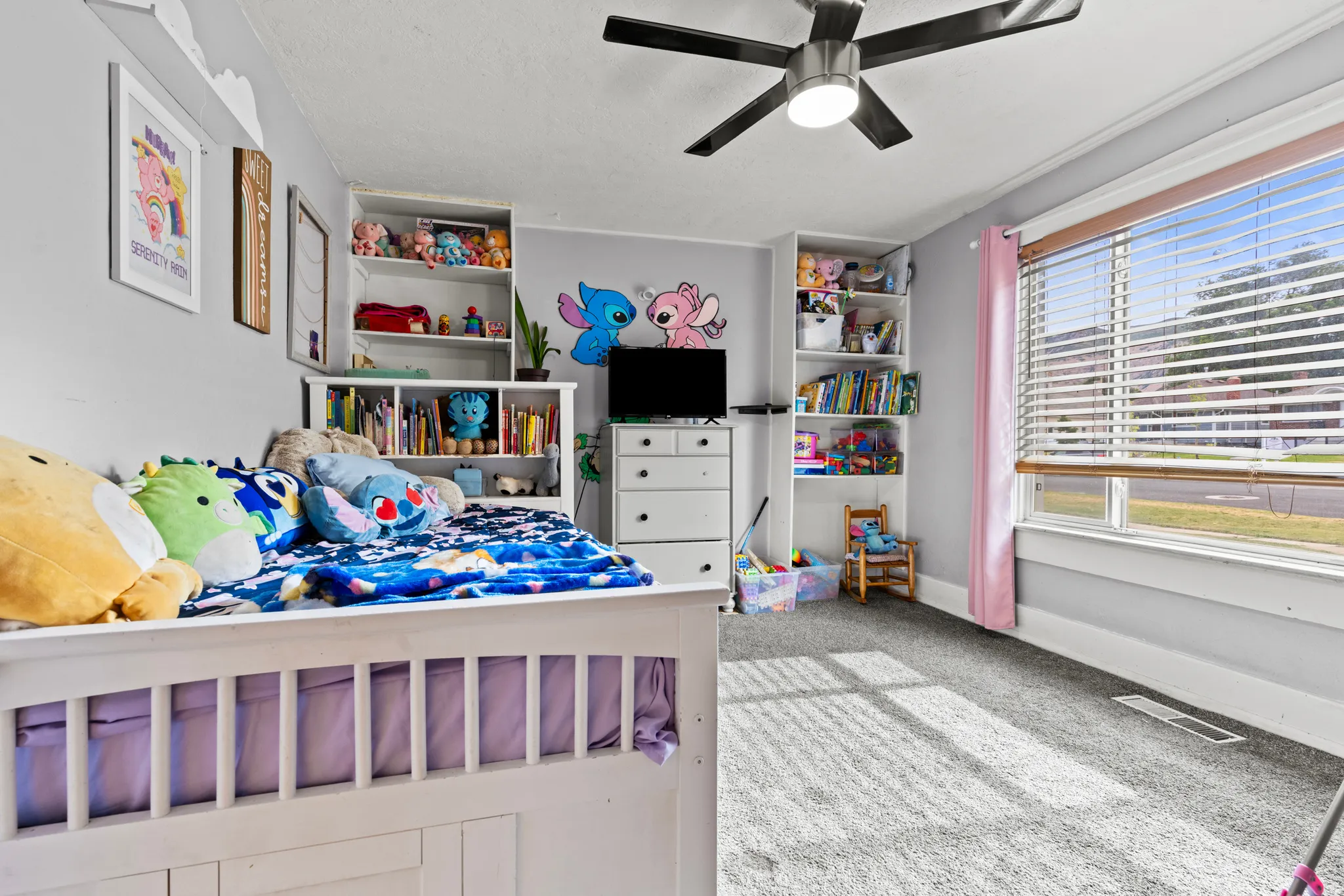 Spacious room featuring light grey walls, grey carpet flooring, and a large window with blinds