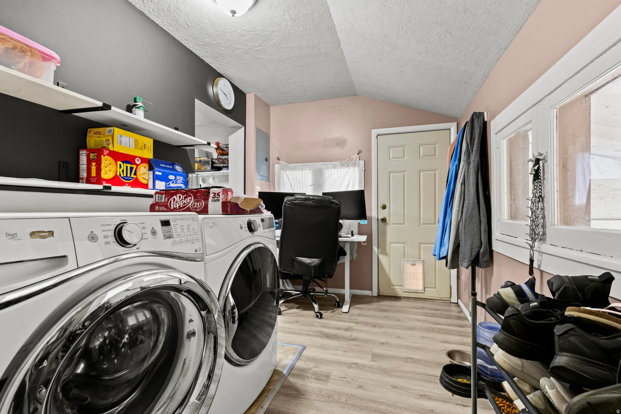 Laundry area with light wood-finish flooring, white built-in shelving, and multiple windows providing natural light