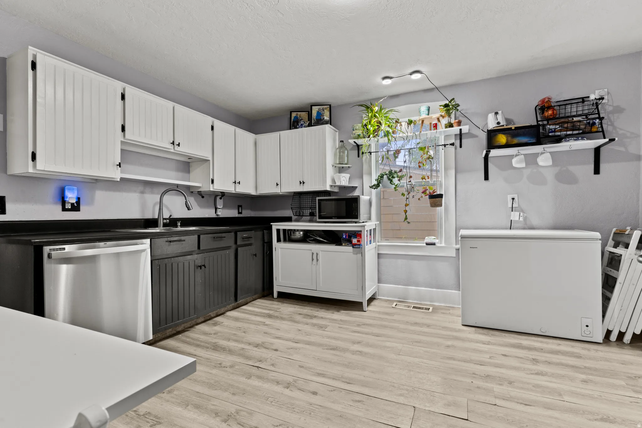 Kitchen featuring wood-finish flooring, two-tone cabinetry with black countertops, and a stainless steel dishwasher