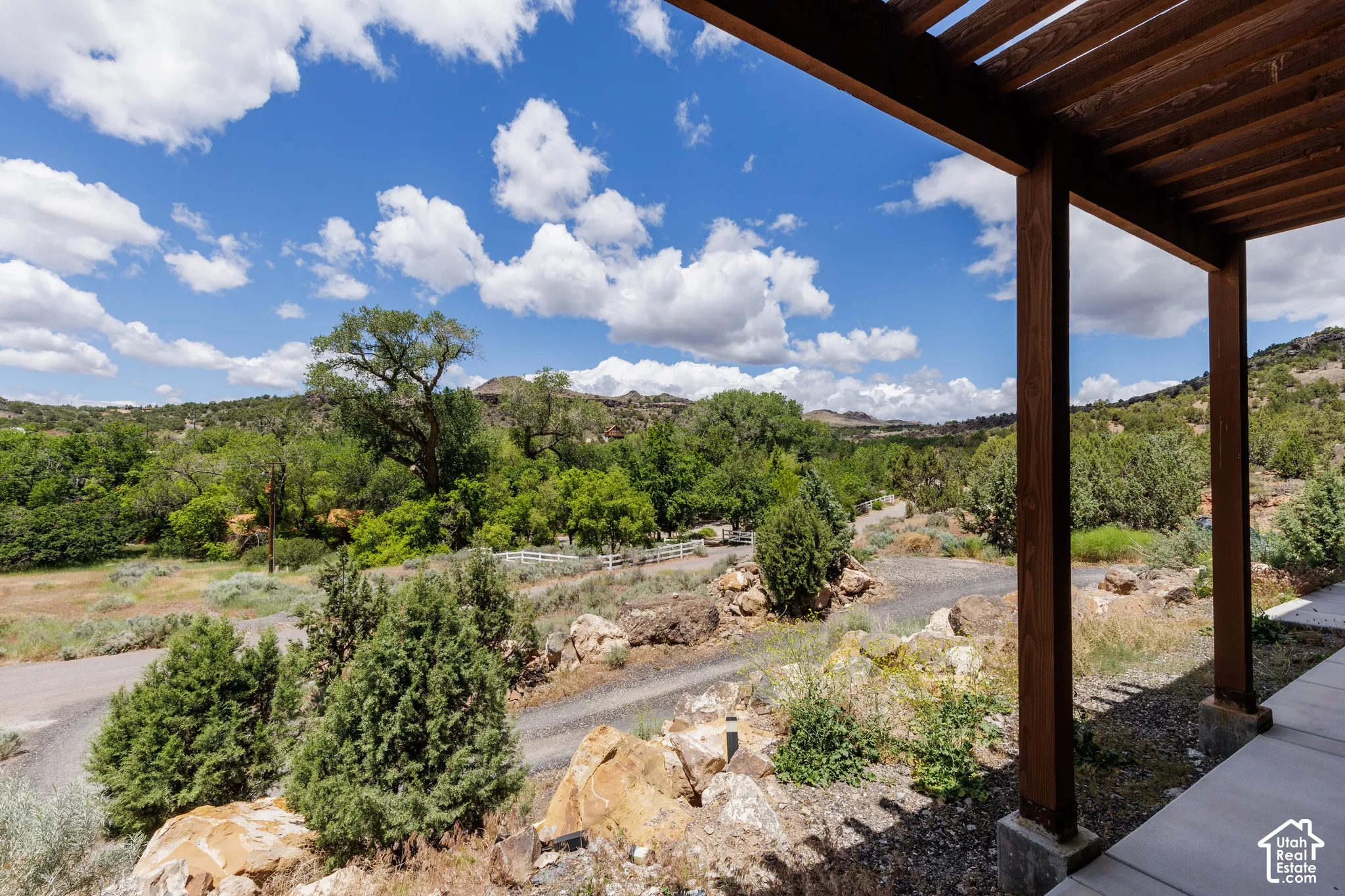 Expansive exterior setting featuring a distant mountain backdrop, mature trees, natural rock formations, and a white fence line