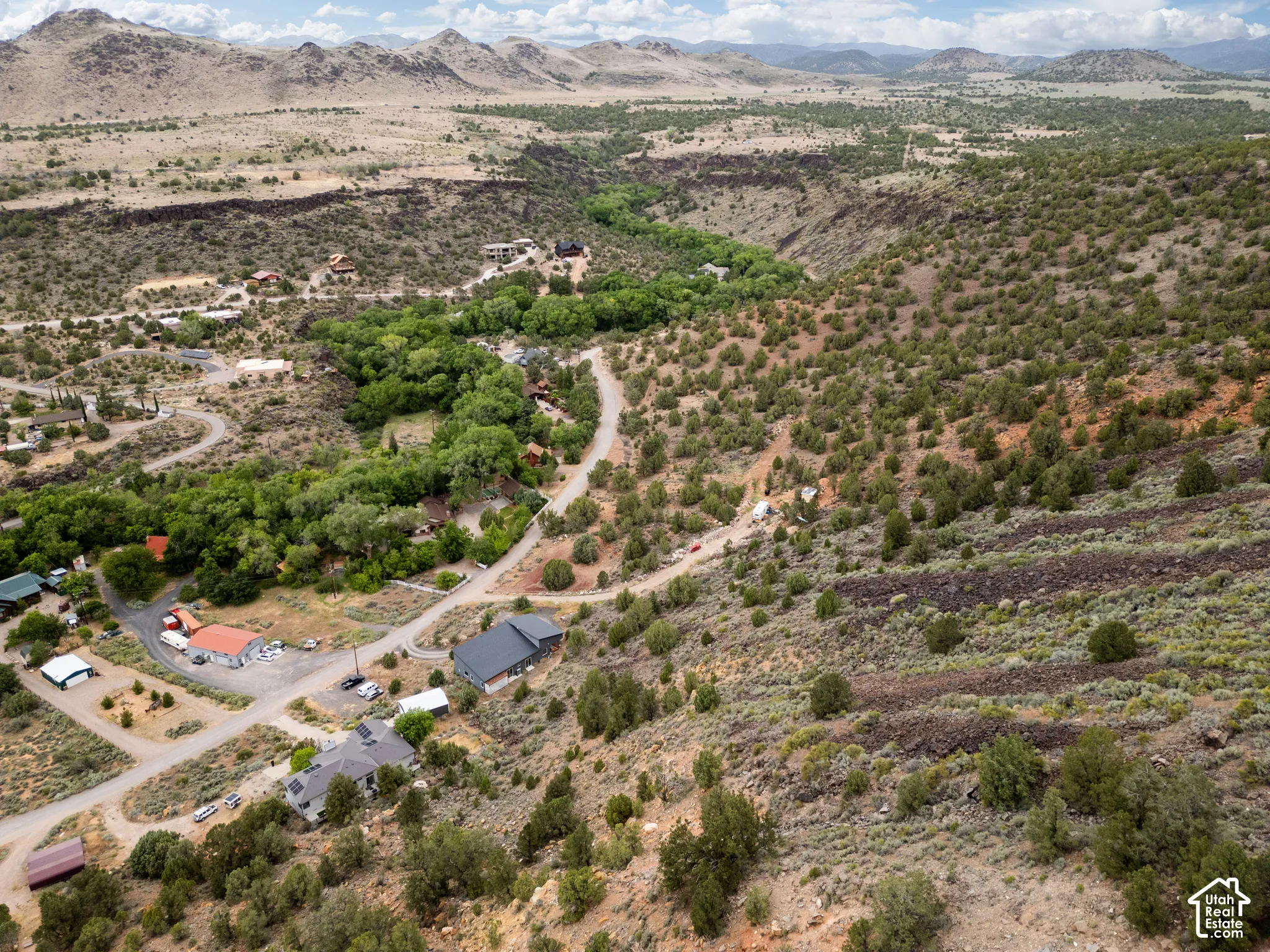 Expansive aerial view of a desert landscape featuring winding roads, scattered residential structures, and a lush green riparian area