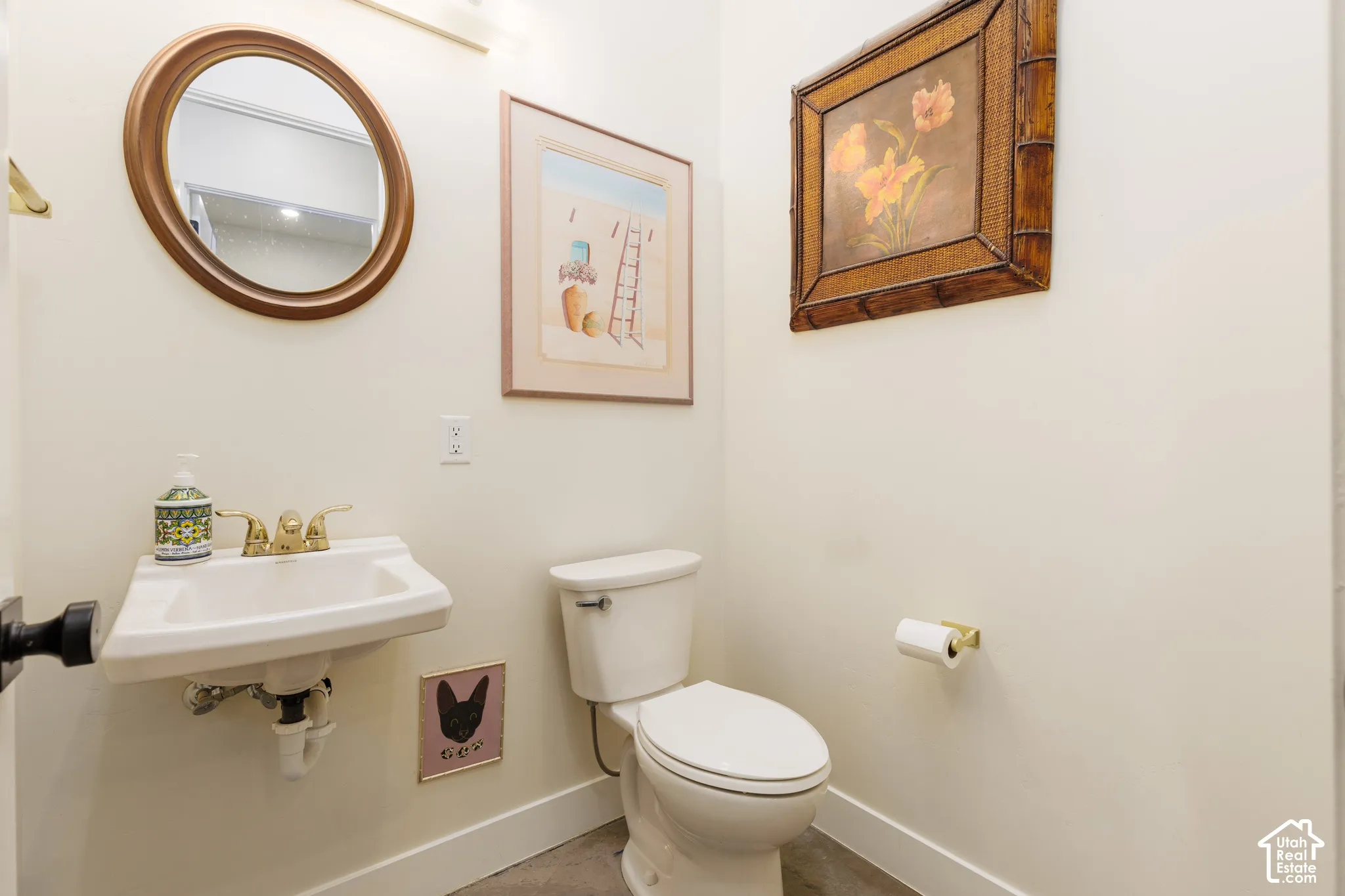 Powder room featuring a circular mirror, pedestal sink with brass-finish faucet, and a white toilet