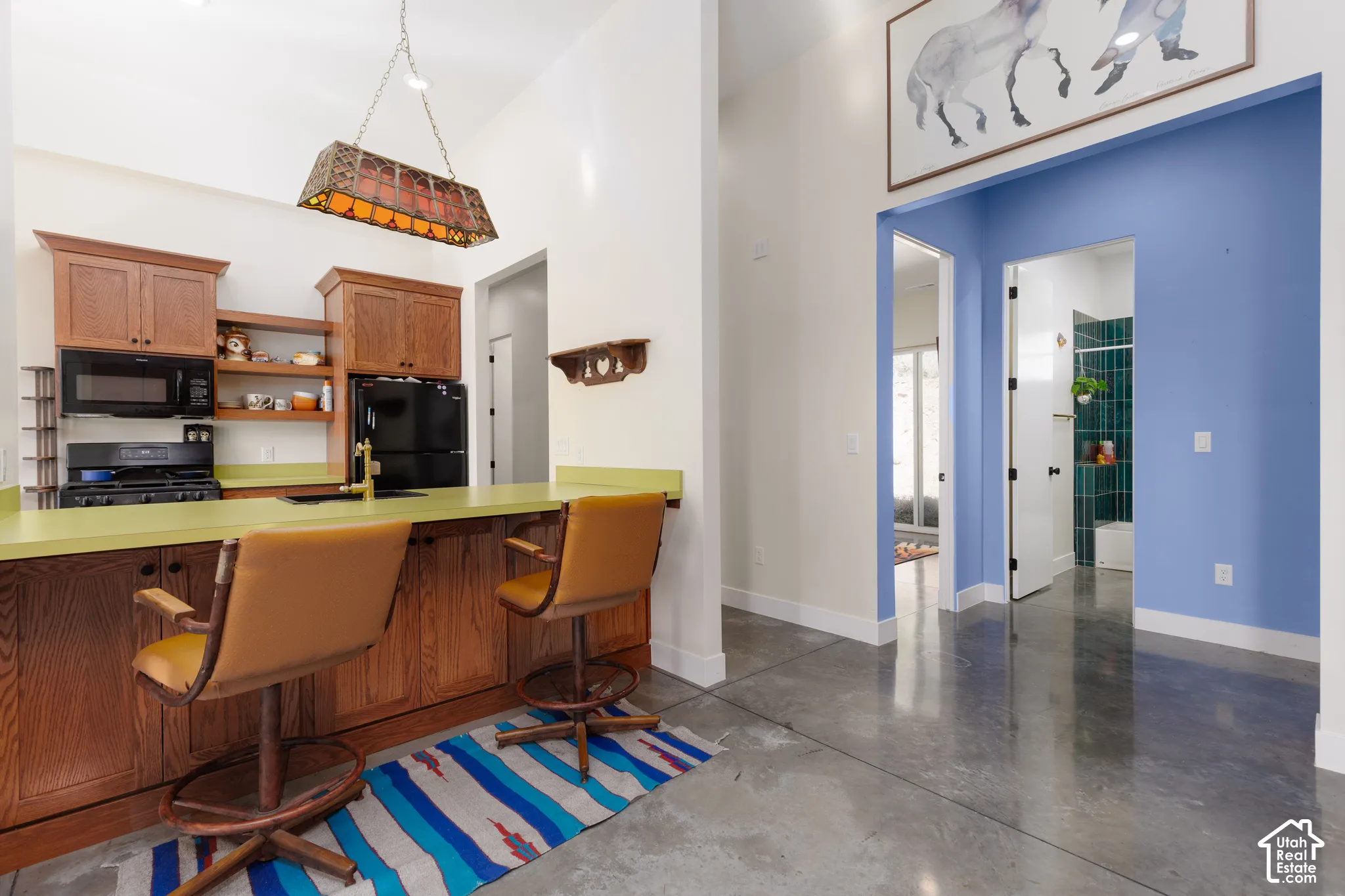 Kitchen area featuring a wood-finish breakfast bar with lime green countertop, upper and lower cabinetry, and black appliances