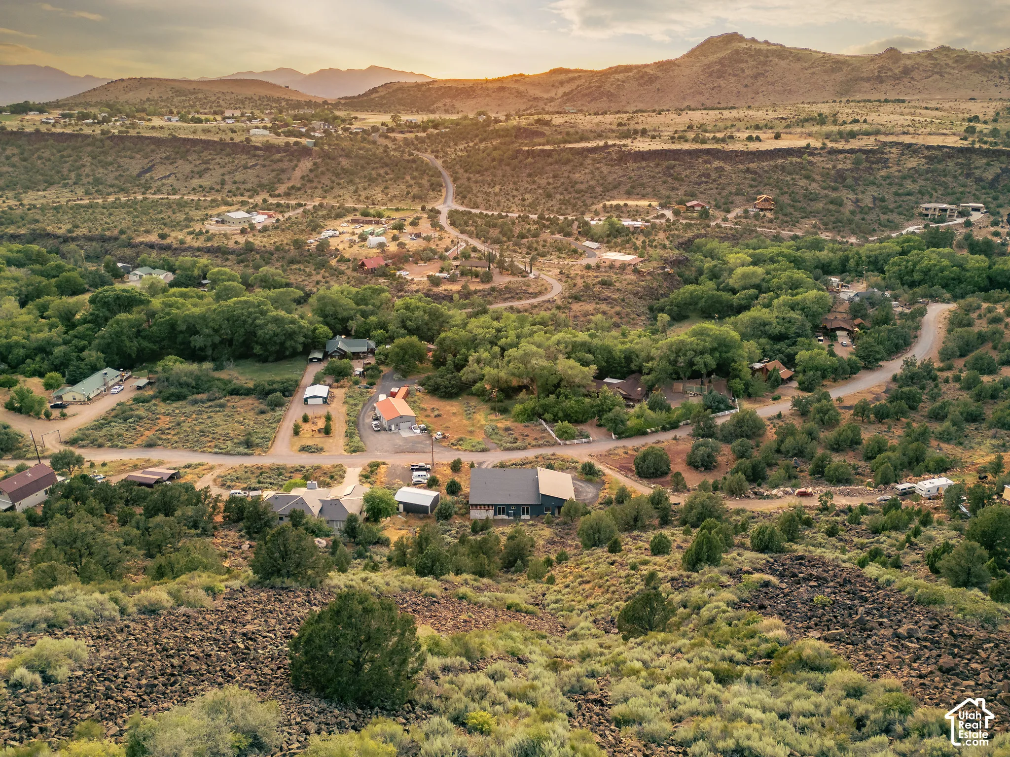 Expansive natural landscape with varied topography featuring distant mountains, established foliage, and multiple residential structures