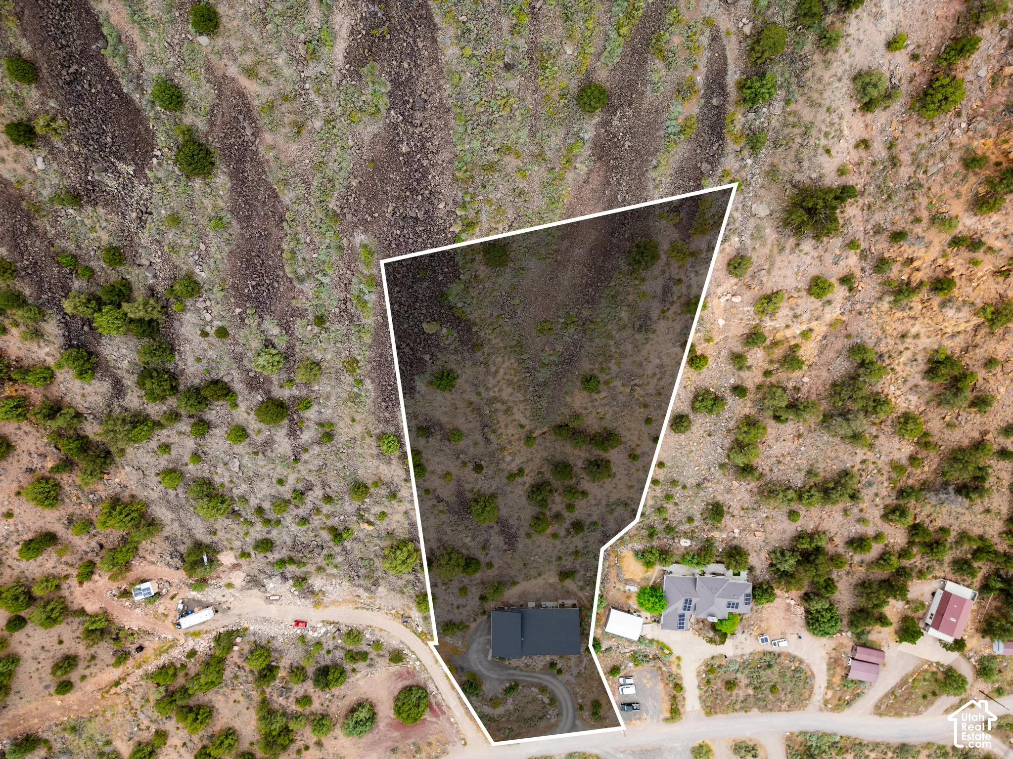 Expansive land parcel featuring a defined property boundary, natural desert landscaping, a single-story residence with a dark roof, a curved driveway, and proximity to an unpaved road
