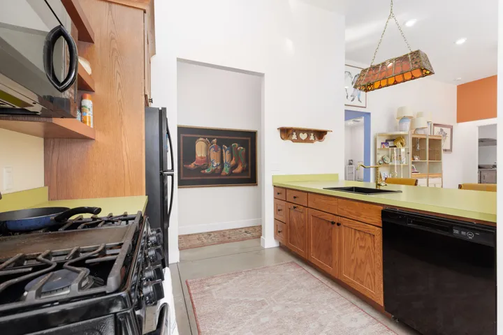 Kitchen featuring wood cabinetry, light green countertops, a black sink with a gold-tone faucet, and a black dishwasher