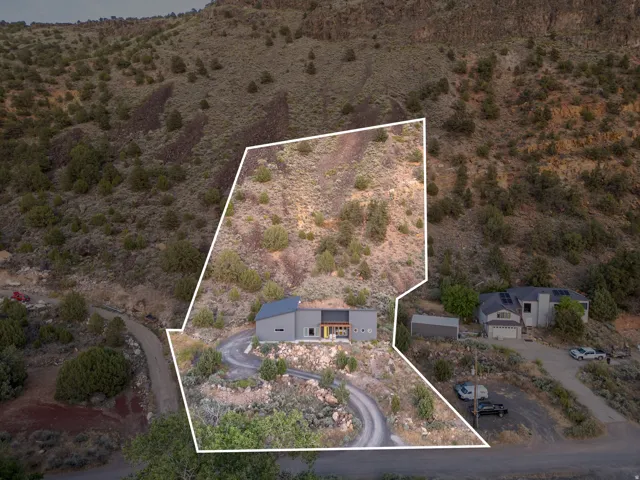 Contemporary hillside residence featuring a gray exterior, a dark-colored roof, a winding driveway, and surrounding natural terrain