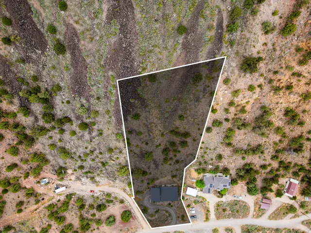 Expansive land parcel featuring a defined property boundary, natural desert landscaping, a single-story residence with a dark roof, a curved driveway, and proximity to an unpaved road