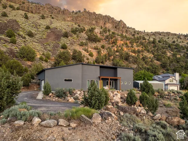 Contemporary grey exterior with a flat roof, featuring a wooden pergola over a patio, round accent windows, and a gravel driveway